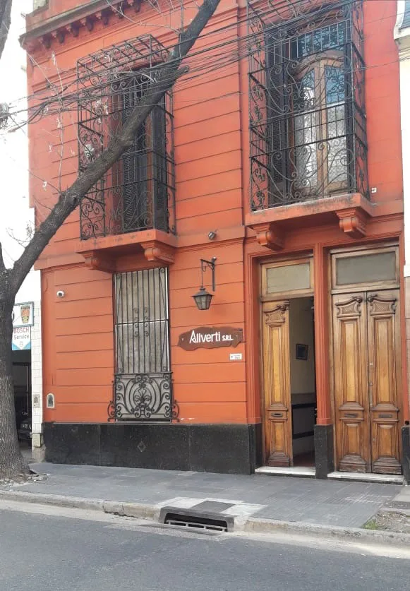 Frente de la sede de Aliverti: una casona de fachada roja, con rejas de hierro y el cartel Aliverti S.R.L. junto a la puerta